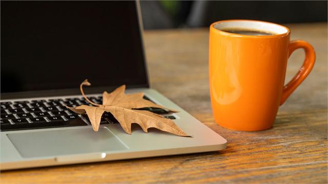 Jesienny liść na laptopie obok kubka kawy